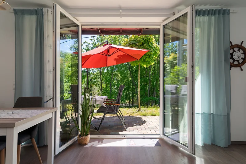Gemütliche Terrasse mit Holztisch, 4 Stühlen Sonnenschirm und Pflanzen.