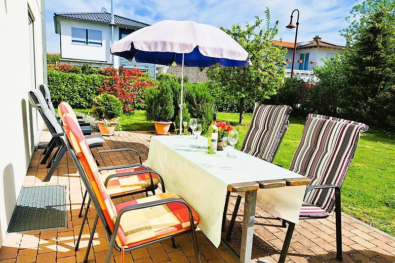 Garten mit Tisch, Stühlen, Sonnenschirm und Blumen.