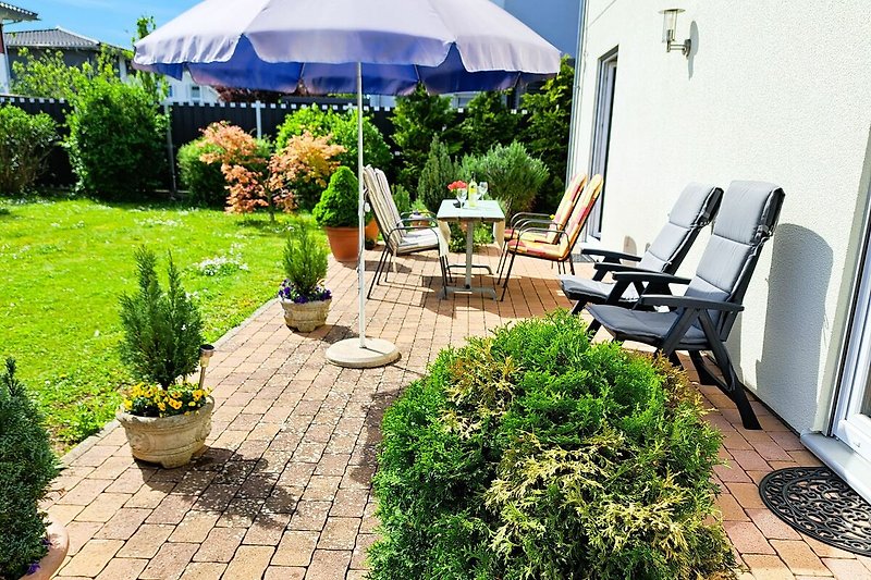 Garten mit Stühlen, Sonnenschirm und Blumen.