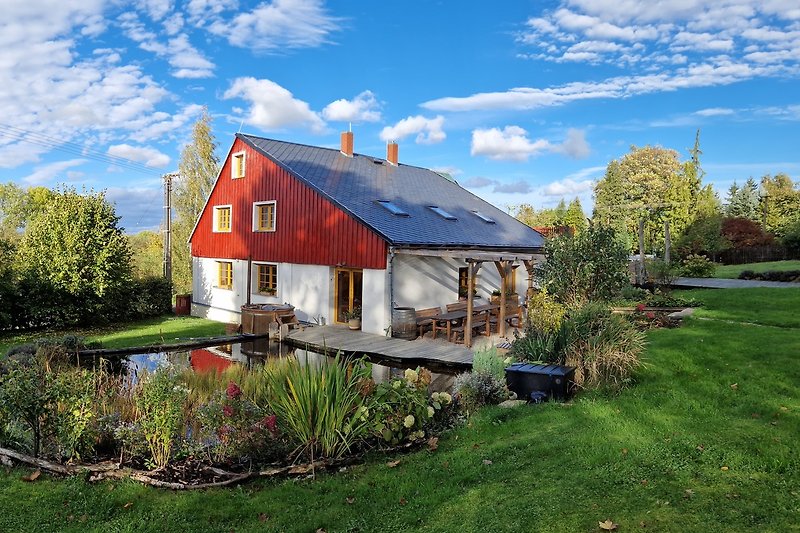 A charming cottage surrounded by lush greenery, with a picturesque sky and beautiful landscaping.