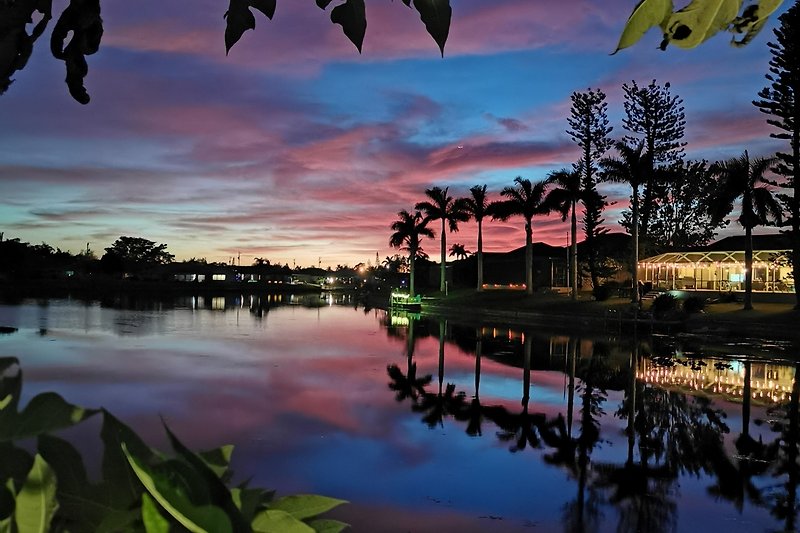 Schönes Ferienhaus am See mit malerischem Sonnenuntergang und tropischer Vegetation.