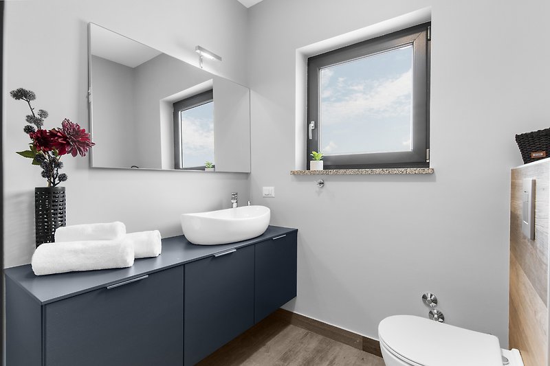 Gemütliches Badezimmer mit Holzboden, Spiegel und Pflanze.