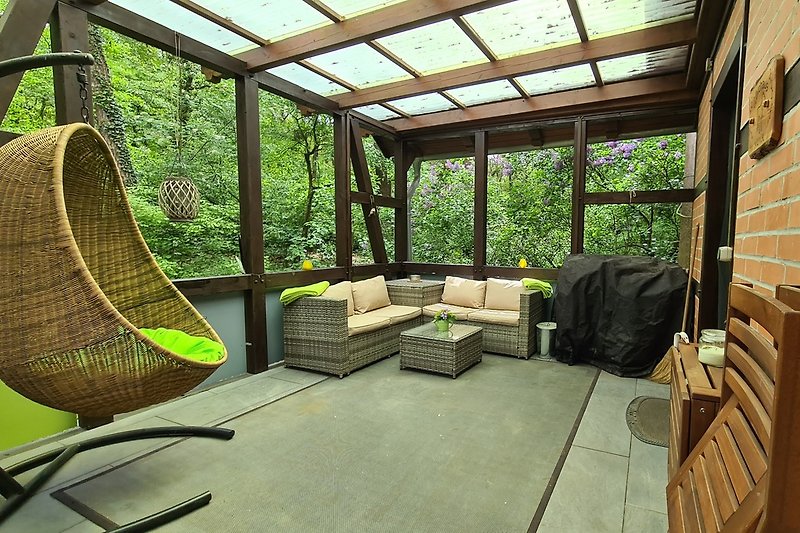 Überdachte Terrasse mit Loungebereich, Gasgrill, Esstisch und Hängesessel.