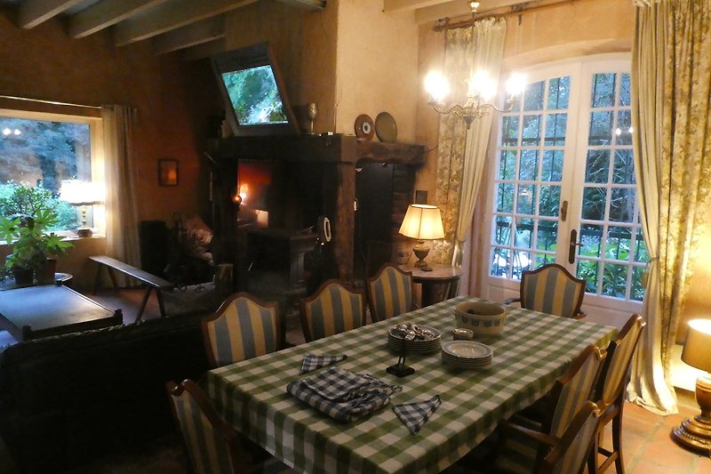 Gemütliches Wohnzimmer mit Holzmöbeln, Tisch und Stühlen, Pflanzen und gemütlicher Beleuchtung.
