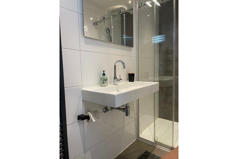 Moderne badkamer met spiegel, kraan, wastafel en glazen douchewand.
