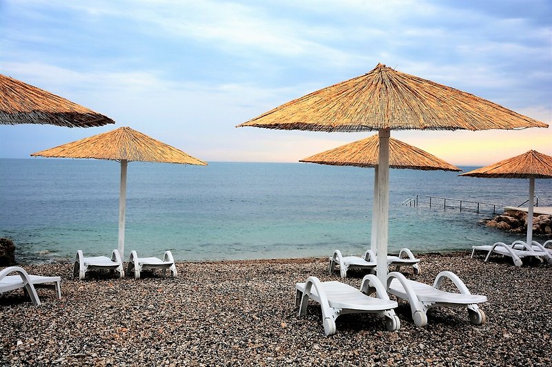 Strand mit Sonnenschirmen, Liegestühlen und Blick aufs Meer.