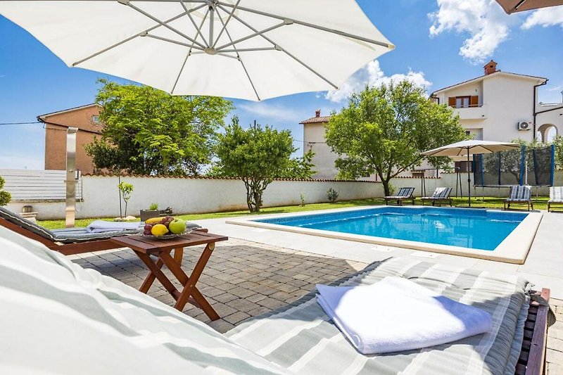 Villa mit Pool, Sonnenliegen und Sonnenschirmen im Garten.