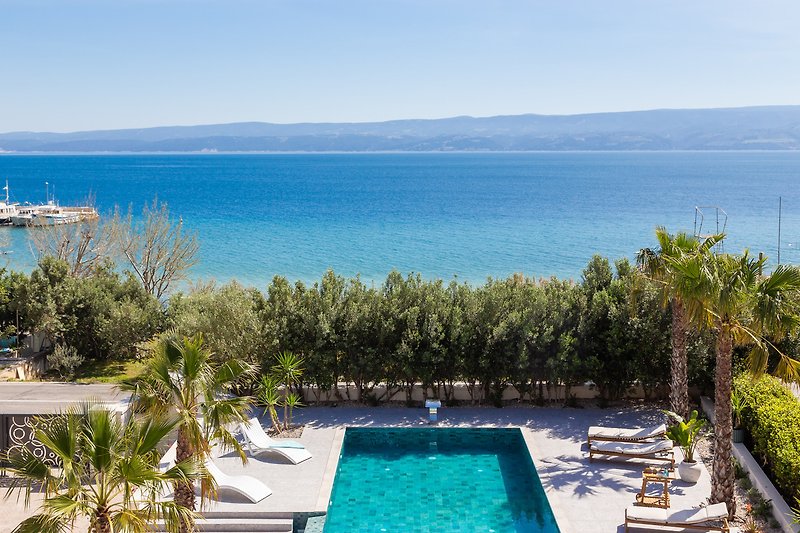 Luxuriöser Pool mit Palmen am Strand und Blick auf das Meer.