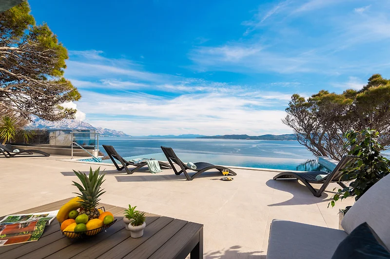 Sonnenterrasse mit Blick auf türkisblaues Meer, Strand und Palmen.
