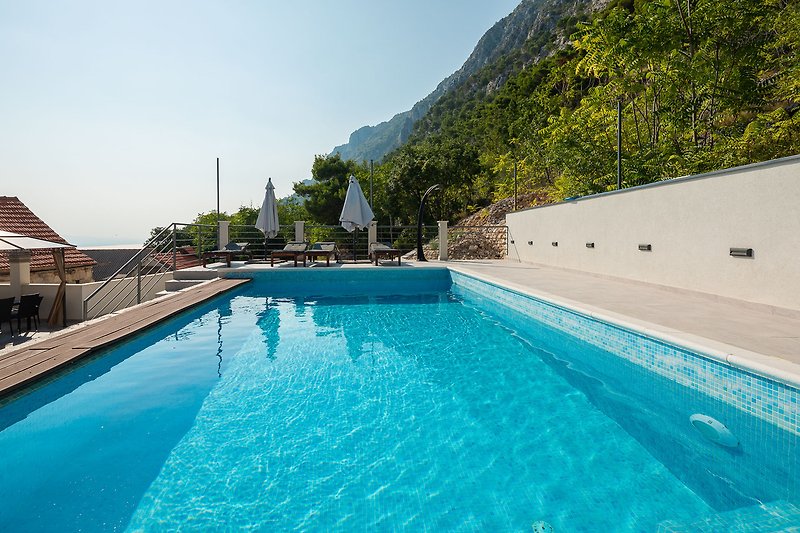 Schwimmbecken mit Blick auf das azurblaue Meer und umgeben von grüner Natur.
