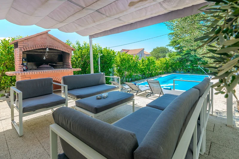 Villa mit Pool, Sonnenliegen und schattiger Terrasse.