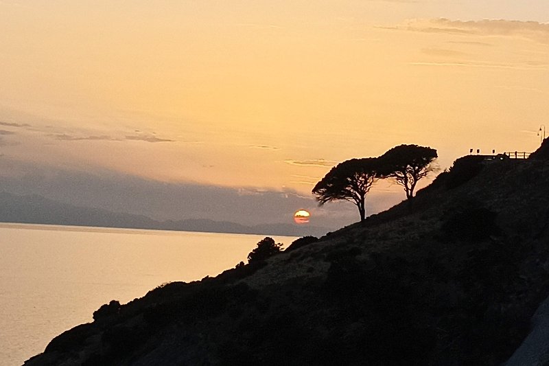 Una vista mozzafiato sul mare al tramonto, con montagne della Corsica e cielo arancione.