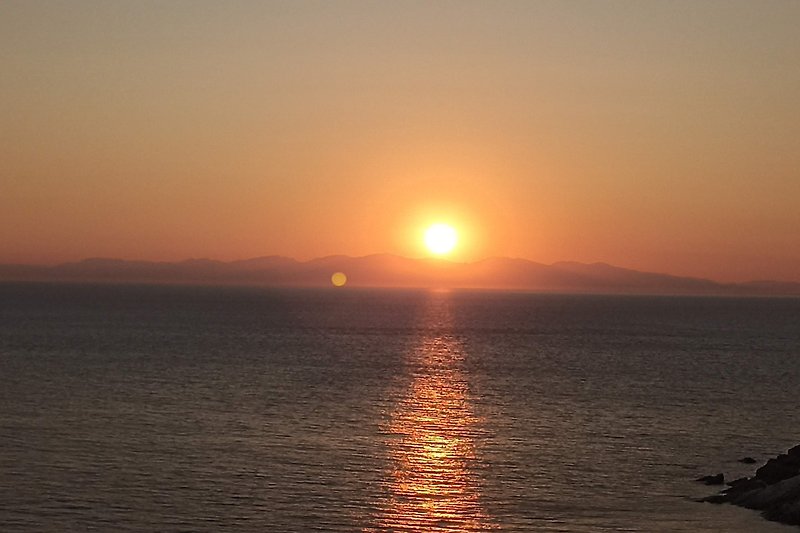 Una vista mozzafiato sul mare al tramonto, con montagne della Corsica  e cielo arancione.