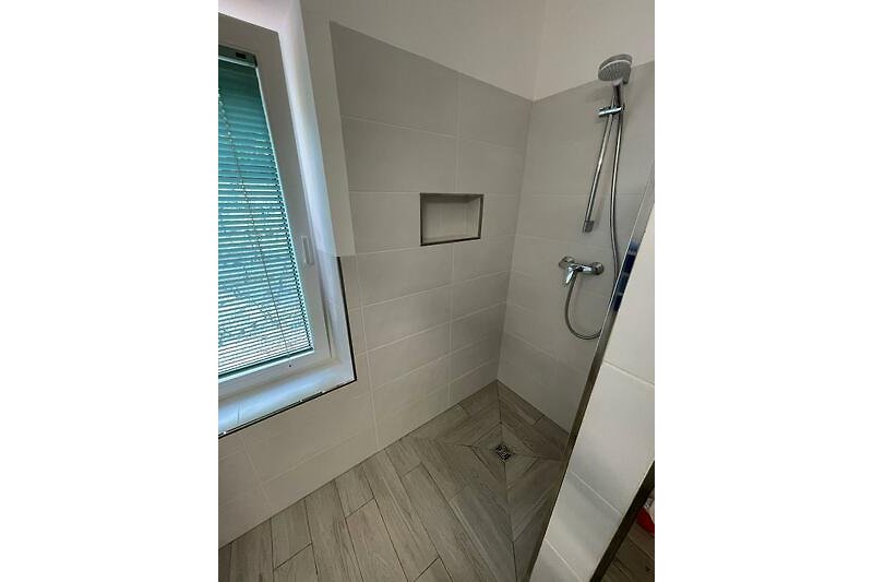 Ein modernes Badezimmer mit Dusche, Fenster und Holzboden.