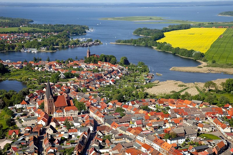 Panoramablick auf Wasser, Natur und die Stadt Röbel, mit grüner Vegetation und blauem Himmel.