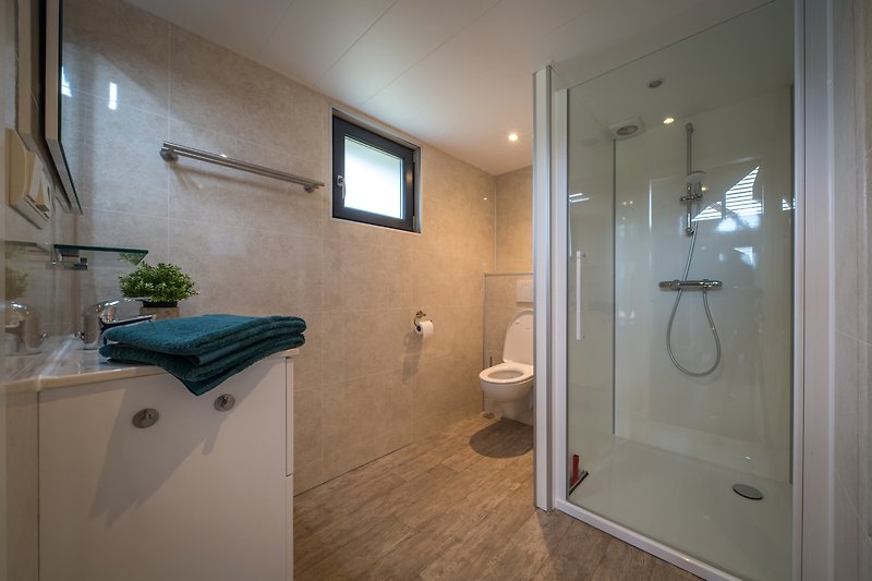 Modernes Badezimmer mit Glasdusche, Holz und Pflanze.