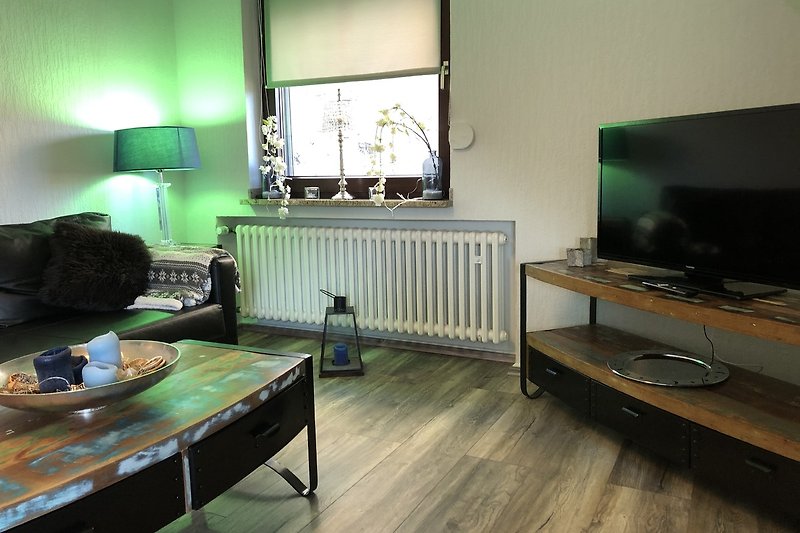 Gemütliches Wohnzimmer mit Holzboden, Fenster und Fernseher.