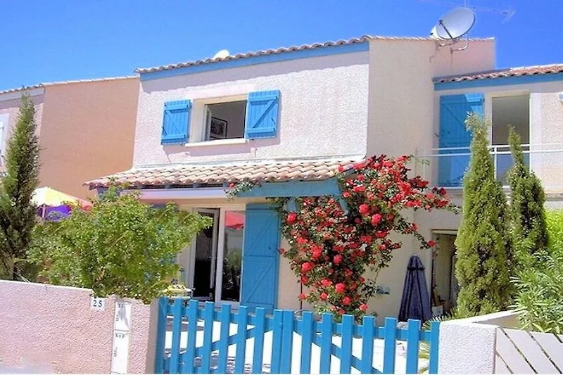 Villa mit Balkon, Palmen, schattigem Vordach und großzügigem Anwesen.