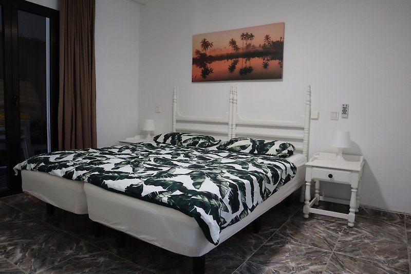 Gemütliches Schlafzimmer mit Holzbett, grauen Textilien und Bilderrahmen.