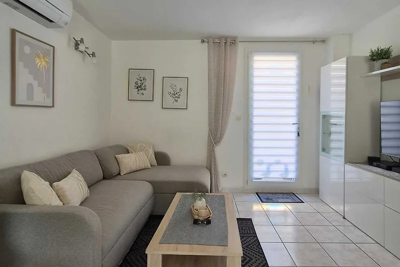 Offener Wohnbereich mit Sofa, Sessel, Couchtisch und großem Fenster.