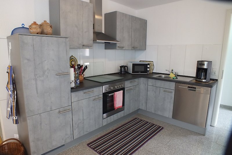 Moderne Küche mit grauen Schränken, Holzboden und modernen Geräten.