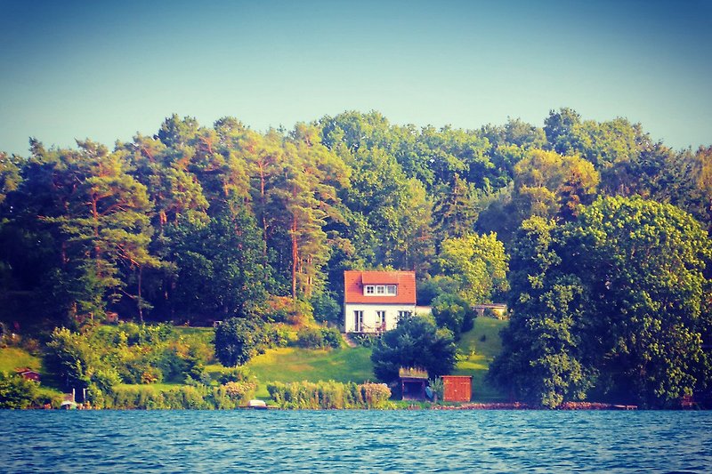 Haus am See mit Blick auf Insel und Wald, ruhige Abendstimmung.