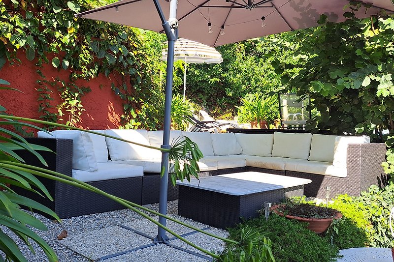 Ein schattiger Außenbereich mit Pflanzen, Möbeln und einem Sonnenschirm.