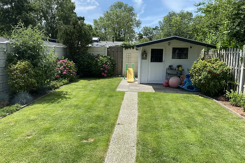 Mooi huis met groene tuin, veranda en bloemen.