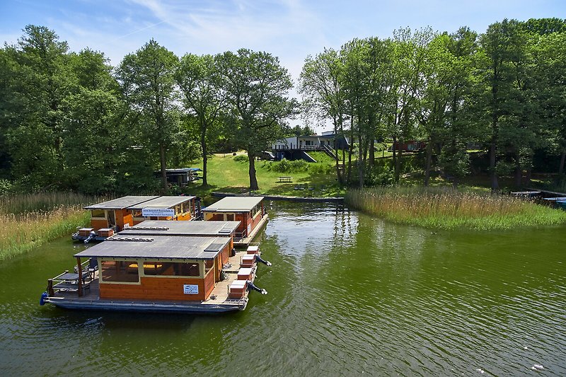 Ein Haus am See mit Boot, grüner Landschaft und wolkenverhangenem Himmel.