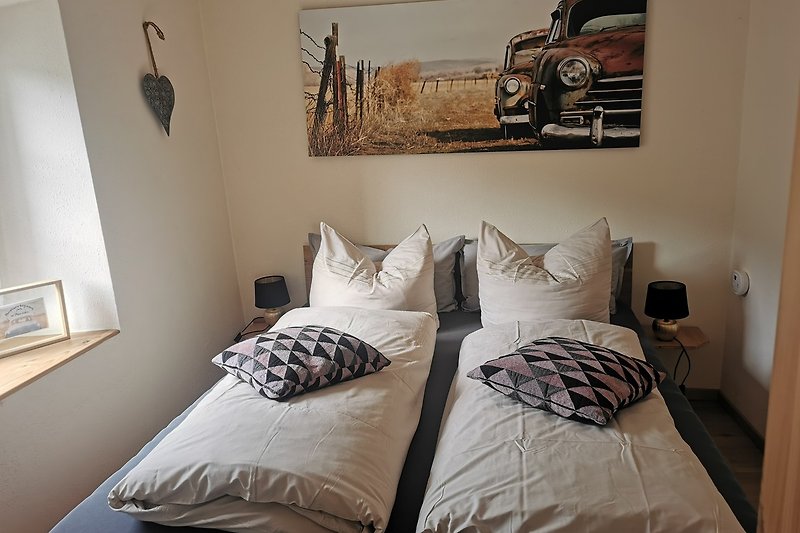 Gemütliches Schlafzimmer mit Holzbett, gemusterten Kissen und Kunst an der Wand