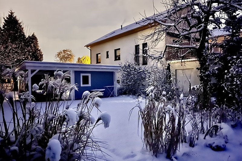 Verschneite Gartenlandschaf mit Eiszapfen und schneebedecktem Dach.