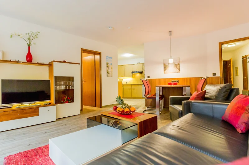 Woonkamer met eethoek, ingebouwde keuken, woonwand met flatscreen-tv.