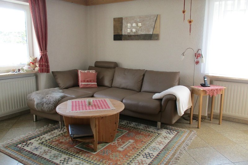 Wohnzimmer mit Holzmöbeln, Sofa, Tisch und Fensterblick.