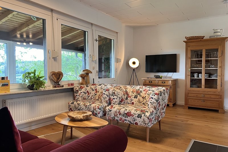 Willkommen in diesem stilvollen Wohnzimmer mit bequemen Möbeln, Pflanzen und einem großen Fenster. Entspannen Sie sich und genießen Sie den Komfort dieses Apartments.