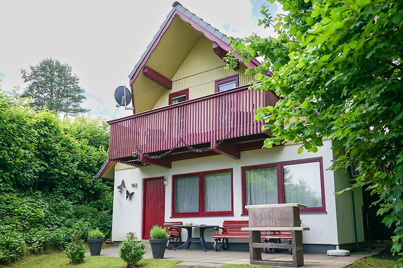 Gemütliches Holzhaus mit Garten, Bäumen und Sitzbank.