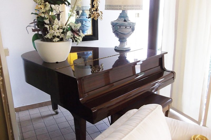 Elegantes Wohnzimmer mit Klavier, Antiquitäten und Blumen.