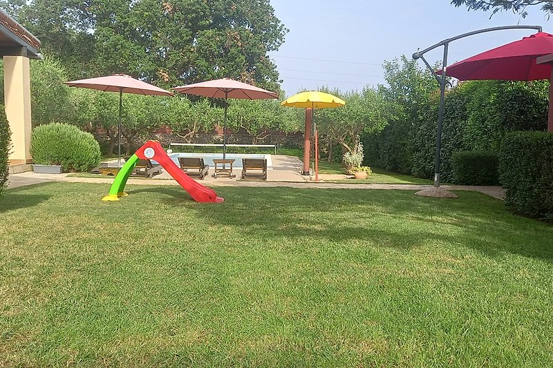 Spielplatz mit Rutsche, Schaukel und Gartenmöbeln im grünen Garten.