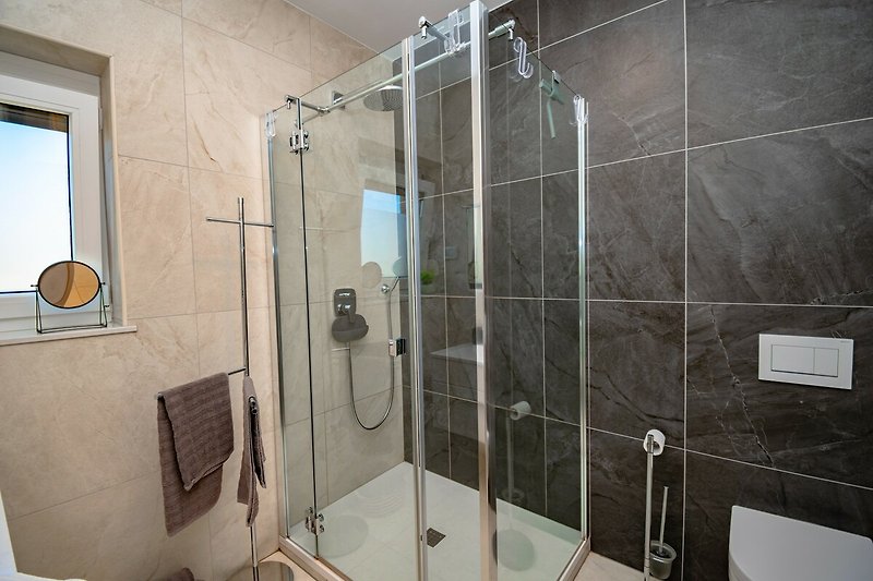 Badezimmer mit Dusche, Spiegel und Waschbecken.