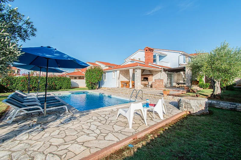 Blaues Wasser, gepflegter Garten und Villa mit Terrasse im Grünen.