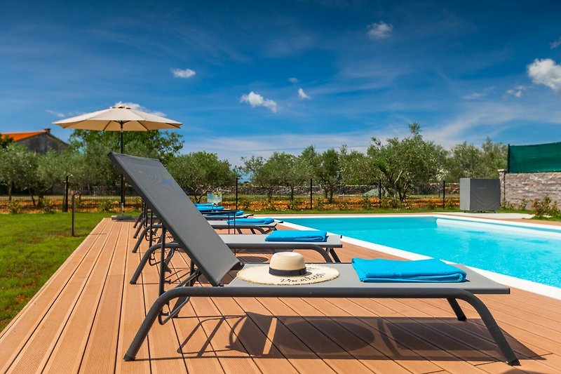 Schwimmbad mit Sonnenliegen und Außenmöbeln in einer blauen Landschaft.