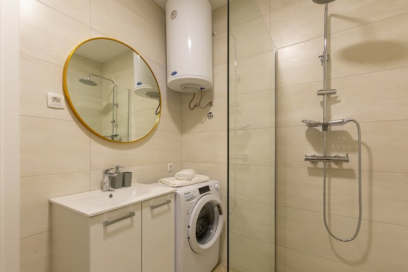 Badezimmer mit Dusche, Waschmaschine, Spiegel und Waschbecken.