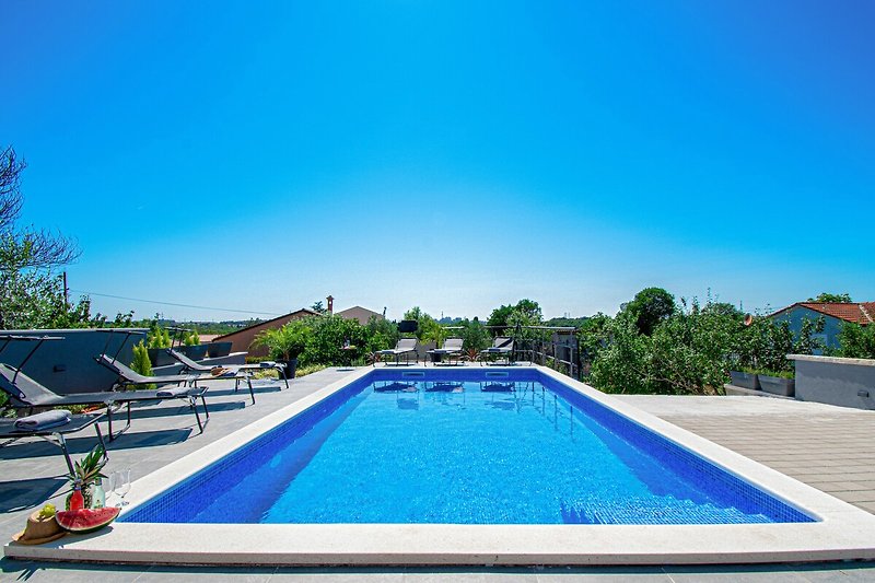 Schwimmbecken mit blauem Himmel und grüner Landschaft.