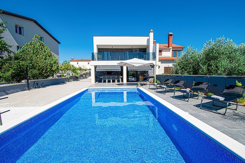 Schönes Ferienhaus mit Pool, blauem Himmel und grünen Pflanzen. Perfekt zum Entspannen und Genießen der Natur.