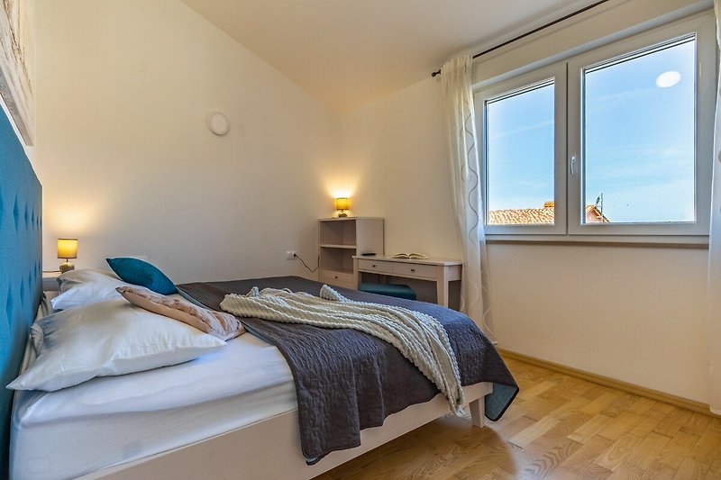 Gemütliches Schlafzimmer mit Holzbett, blauem Fenster und bequemer Einrichtung.