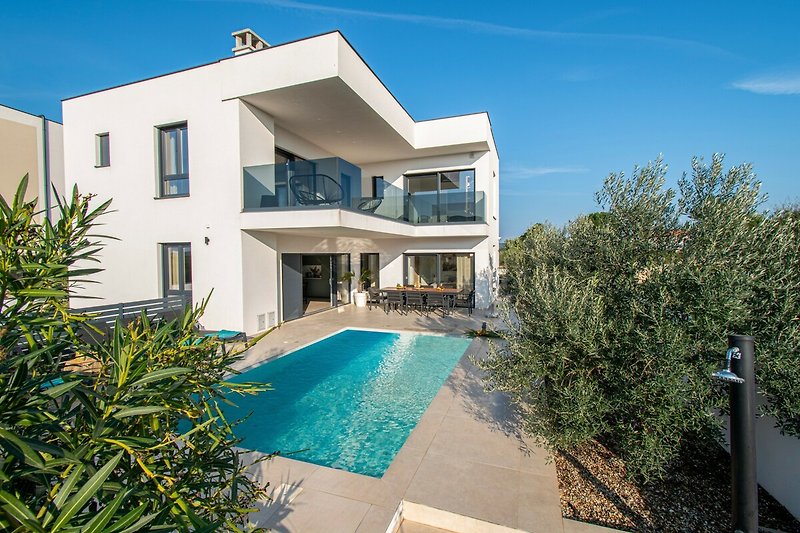 Luxuriöse Villa mit Pool, umgeben von Palmen und blauer Himmel.