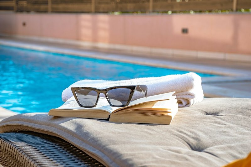 Schwimmbad mit Sonnenbrillen, blauem Wasser und bequemen Liegen.