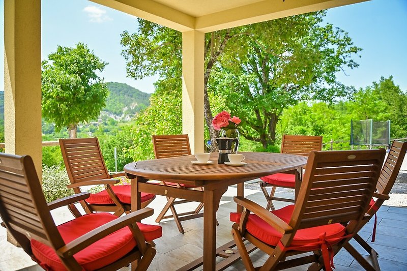 Holzterrasse mit gelbem Tisch, Stühlen, Pflanzen und Sonnenschirm.