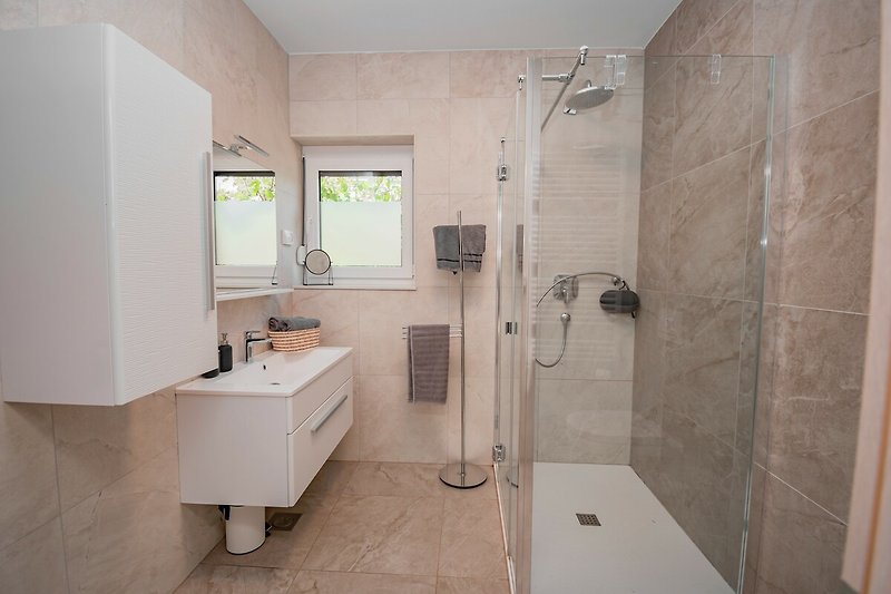 Badezimmer mit Spiegel, Waschbecken, Dusche und Fenster.