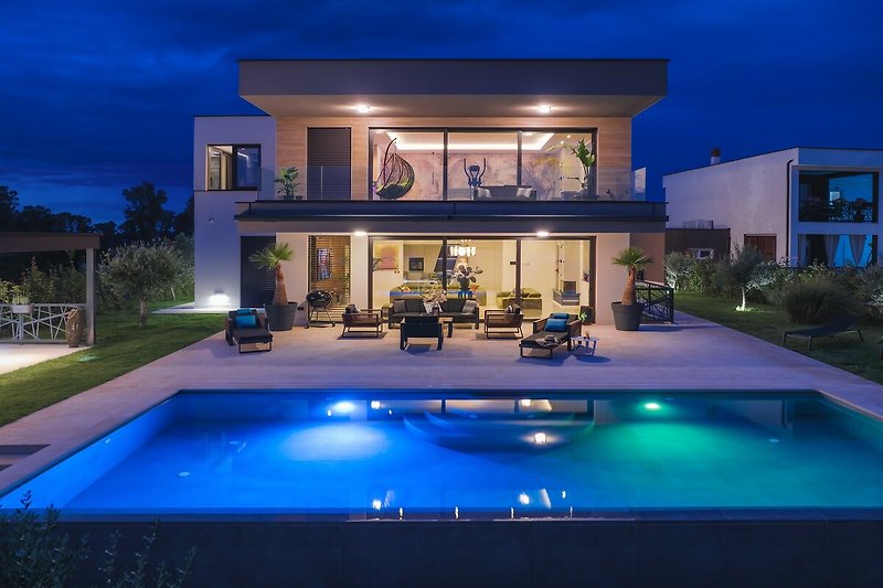 Schwimmbad mit blauem Wasser, umgeben von Pflanzen und einem schönen Haus.