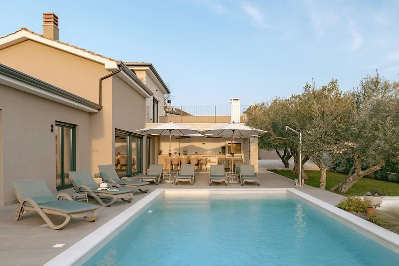 Sonnenterrasse mit Pool, Liegen, Schirmen und Blick auf Villen.